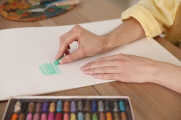 Woman drawing picture with bright wax crayons on paper at wooden table in artist's studio, closeup