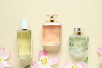 Bottles of perfume and beautiful flowers on beige background, flat lay