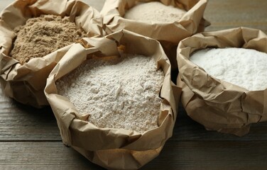 Different types of flour in paper bags on wooden table, closeup