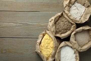 Different types of flour in paper bags on wooden table, flat lay. Space for text