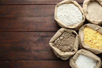 Different types of flour in paper bags on wooden table, flat lay. Space for text