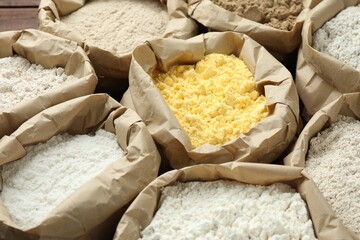 Different types of flour in paper bags on wooden table, closeup