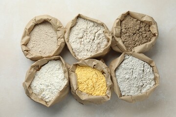 Different types of flour in paper bags on white table, flat lay