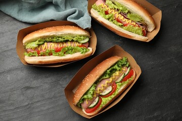 Tasty hot dogs with vegetables on black table, flat lay