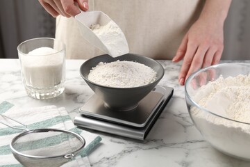 Woman putting sugar into bowl on digital kitchen scale at white marble table, closeup