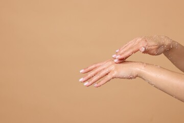 Fototapeta premium Woman applying body scrub onto her hands on beige background, closeup. Space for text