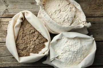 Different types of flour in bags on wooden table, flat lay