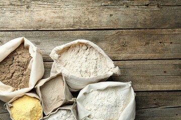 Different types of flour in bags on wooden table, flat lay. Space for text