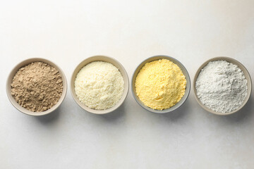 Different types of flour in bowls on light grey table, flat lay