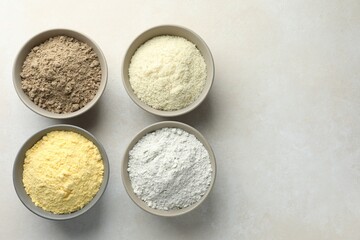 Different types of flour in bowls on light grey table, flat lay. Space for text