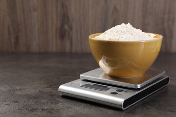Digital kitchen scale with bowl of flour on grey table, closeup. Space for text