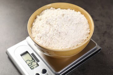 Digital kitchen scale with bowl of flour on grey table, closeup