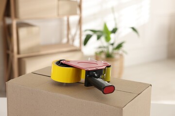 Dispenser with adhesive tape on cardboard box indoors, closeup