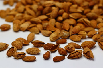 Raw almonds with shells scattered on a white surface, showcasing their natural texture