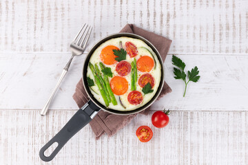 Fried eggs with vegetables asparagus, onions, tomatoes in a frying pan on a white background. Top view.