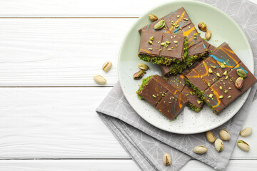 Pieces of Dubai chocolate bars with pistachios and knafeh on white wooden table, flat lay. Space for text