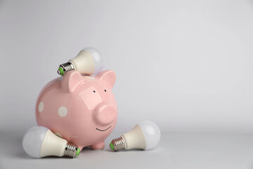 Piggy bank and light bulbs on grey background, space for text. Energy saving concept