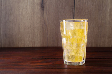 Sweet soda water with ice cubes in glass on wooden table, space for text