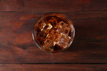 Sweet soda water with ice cubes in glass on wooden table, top view