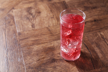 Sweet soda water with ice cubes in glass on wooden table, space for text