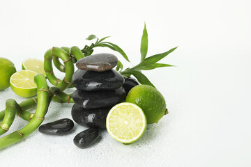 Spa composition with limes, massage stones and bamboo stems on wet surface against white background, space for text