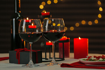 Red wine, burning candles and gift box on table. Romantic dinner