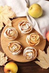 Freshly baked apple roses, fruits and dry leaves on wooden table, flat lay