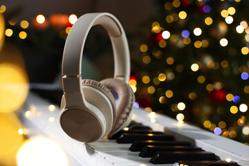 Headphones on electric piano against Christmas tree with blurred lights, closeup. Bokeh effect