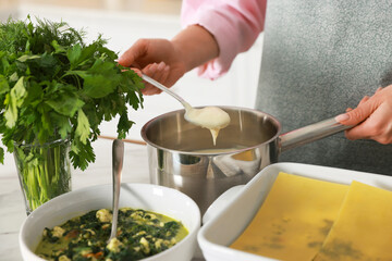 Woman making spinach lasagna at table indoors, closeup