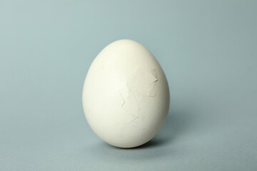 One egg with cracked shell on light grey background, closeup