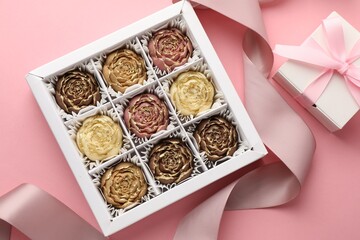 Flower shaped chocolate bonbons in box, gift and ribbon on pink background, flat lay