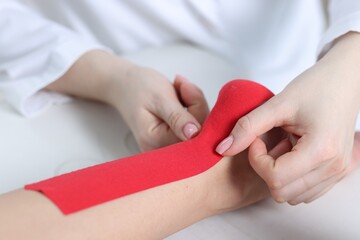Doctor applying kinesio tapes to patient's foot in hospital, closeup