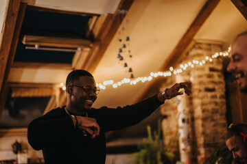 Friends enjoying a lively indoor gathering with string lights, cheerful atmosphere, and camaraderie.