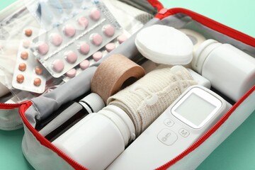 First aid kit. Different medical supplies in bag on turquoise background, closeup