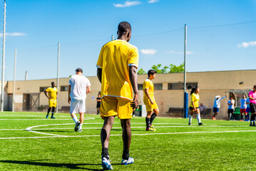 Fototapeta premium young black african american man playing a match in a football pitch on a sunny day with a mixed race team. Young athlete practicing soccer doing sport and exercise