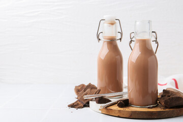 Tasty chocolate milk in glass and pieces of chocolate on white tiled table, closeup. Space for text