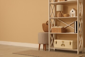 Shelving unit with decor, stool and wicker bag near beige wall indoors, space for text