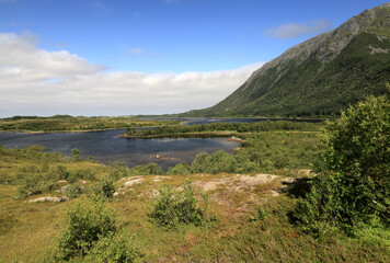 Landscape photo with a view of the mountains and a bay of water against a blue sky with clouds in the Lofoten Islands in Norway