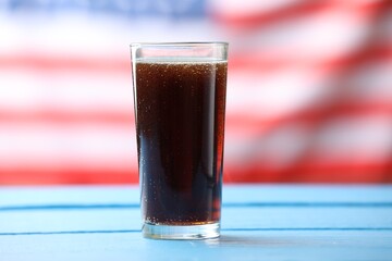 Glass of soda drink on blue wooden table against American flag, closeup