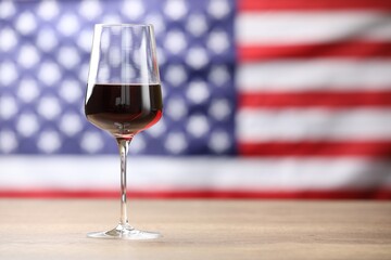 Glass of wine on wooden table against American flag. Space for text