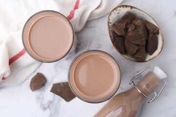 Tasty chocolate milk in glasses, bottle and pieces of chocolate on white marble table, flat lay