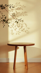 A simple wooden table with a round top filled with a coating that provides sunlight. The delicate shadows of leafy branches play on the textured cream wall in the background.