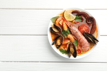 Delicious seafood soup in bowl on white wooden table, top view. Space for text