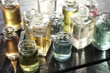Perfume bottles with aromatic oils on black wooden background, closeup