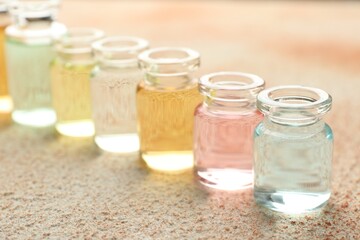 Perfume bottles with aromatic oils on beige textured background, closeup