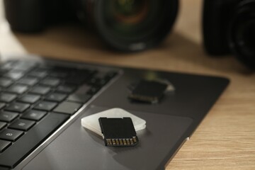 SD memory cards, holder, laptop and photo camera on wooden table, closeup
