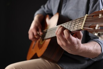 Obraz premium Man playing guitar on black background, focus on hand