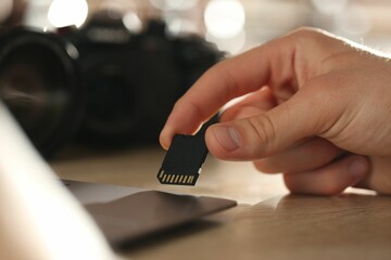 Man inserting SD memory card into laptop at wooden table indoors, closeup