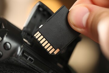 Man inserting SD memory card into photo camera indoors, closeup