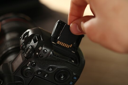 Man inserting SD memory card into photo camera indoors, closeup